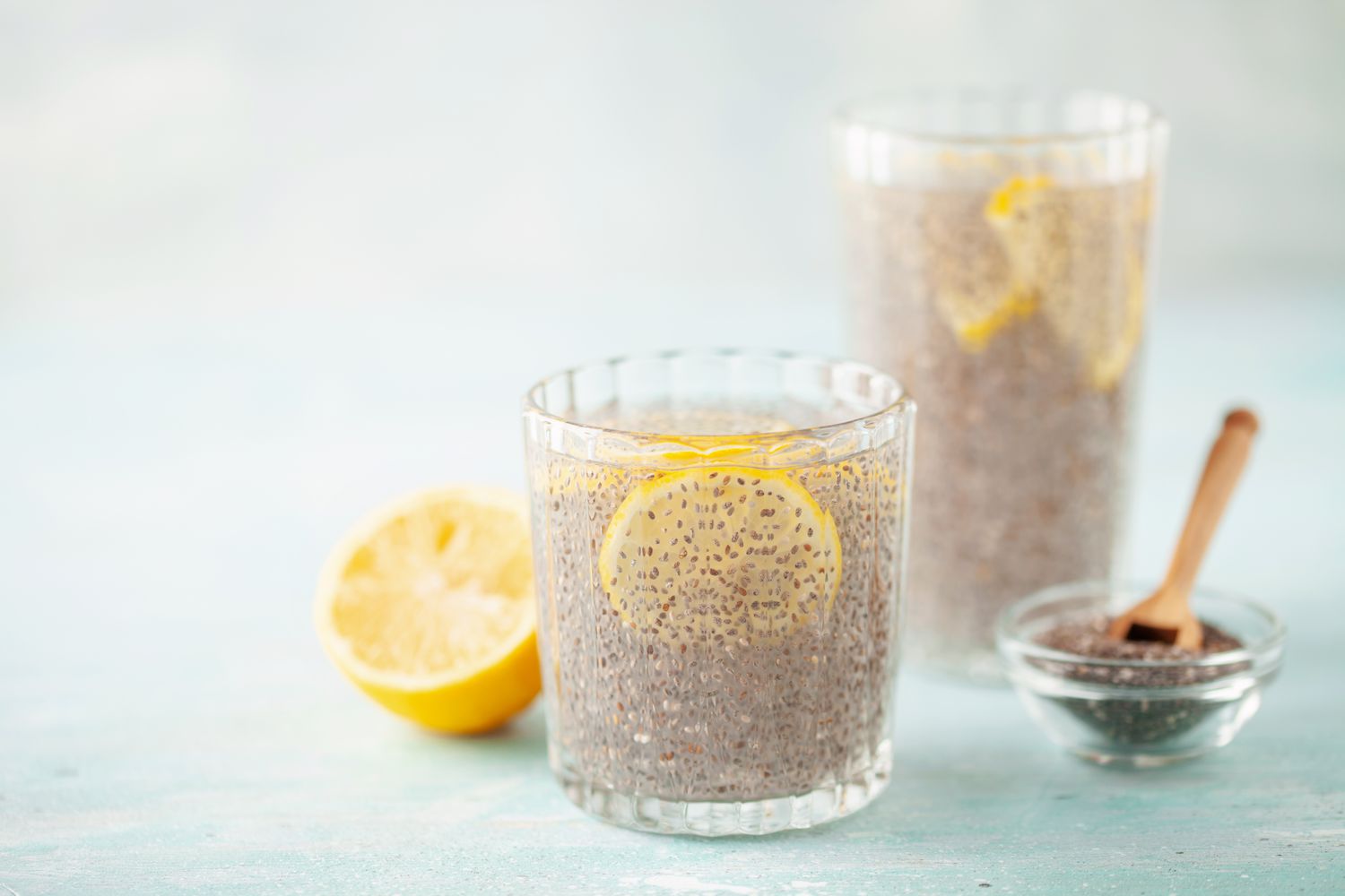 Two glasses of chia seed water with lemon slices, a lemon half, and a bowl of chia seeds with a spoon on the side