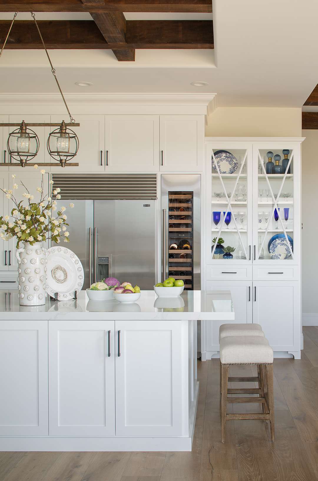 Kitchen interior featuring a large island, stools, white cabinetry, an integrated refrigerator, and decorative elements including glassware