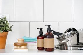 Two labeled pump bottles next to a brush towels and kitchen pots on a white countertop