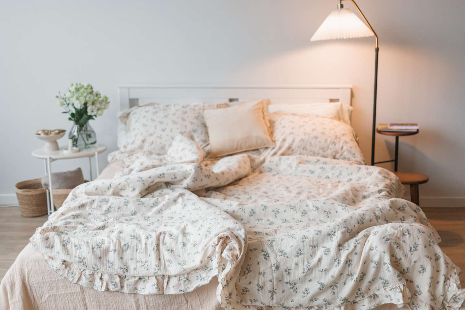 A neatly arranged bed with patterned bedding surrounded by a small table with a floral arrangement and a lamp in a cozy room