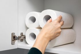 A hand reaches into a cabinet to pick up a roll of paper towels