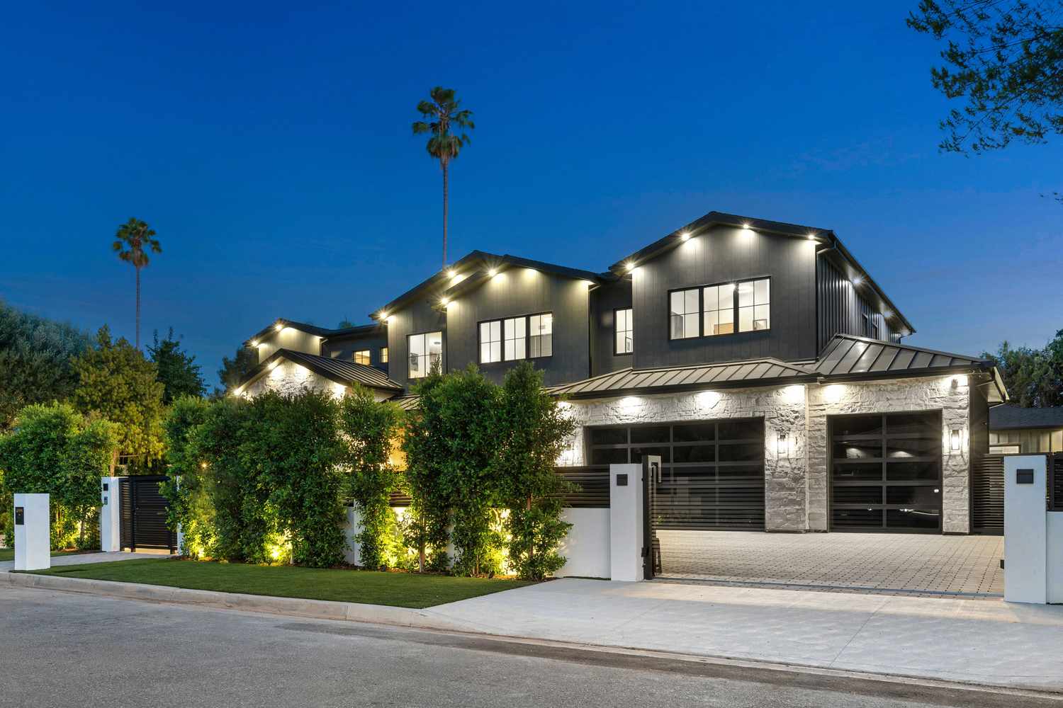 Modern twostory house with prominent lighting multiple garage doors and a driveway at dusk