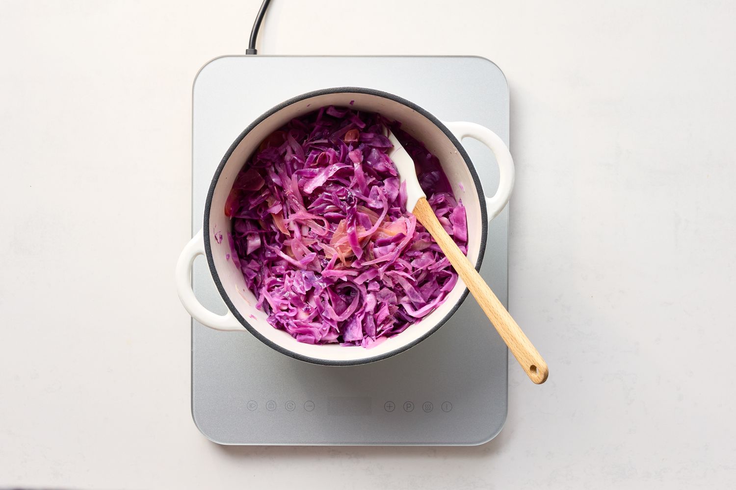 A pot of cooked braised red cabbage with a wooden spoon on a countertop