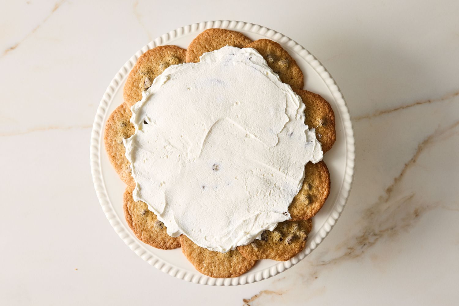 Icebox cake made with stacked chocolate chip cookies and topped with cream on a stand