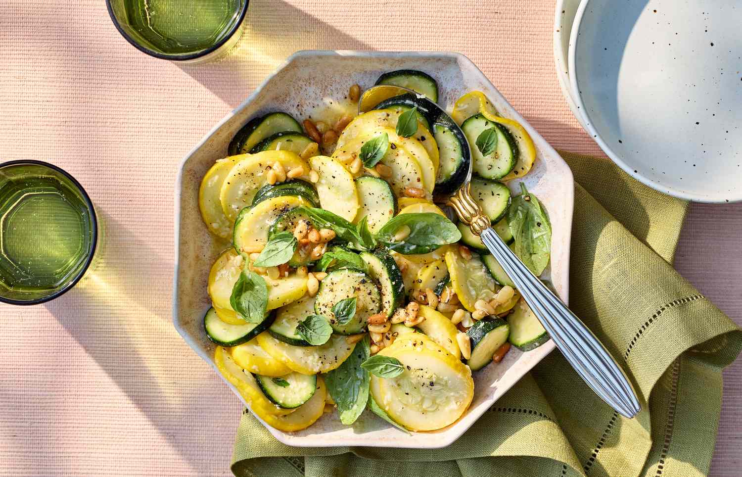 A prepared zucchini and squash salad in a bowl with visible garnishes and a serving utensil