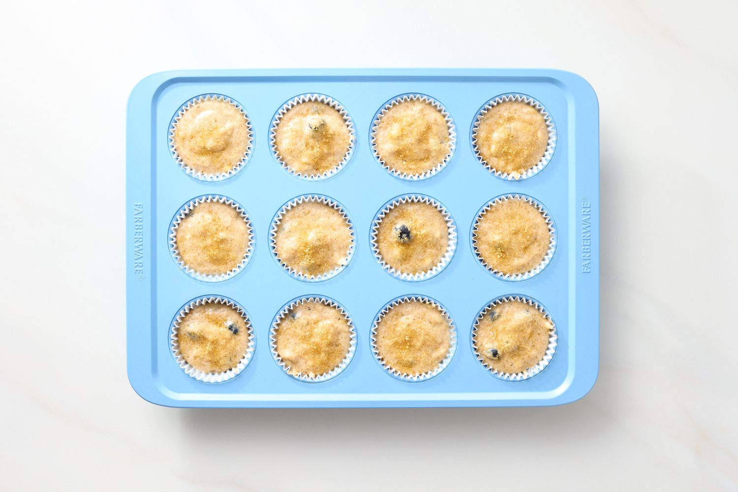 A muffin tray with twelve uncooked vegan blueberry muffins in paper liners prepared for baking