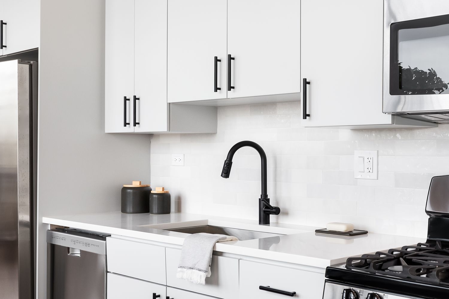 A modern kitchen counter and sink setup a black faucet and minimalistic appliances organized around it
