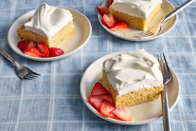 portions of tres leches cake topped with whipped cream, with strawberries on the side