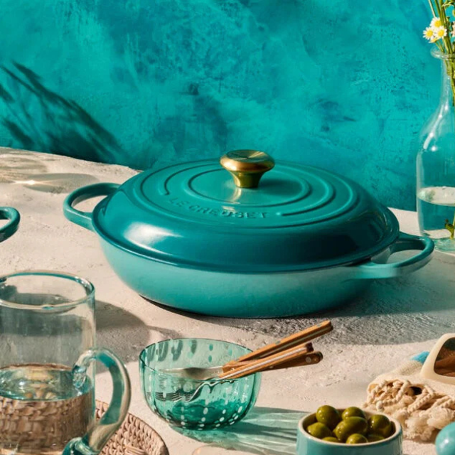 A cast iron cooking pot with a lid on a table surrounded by tableware and decorative items