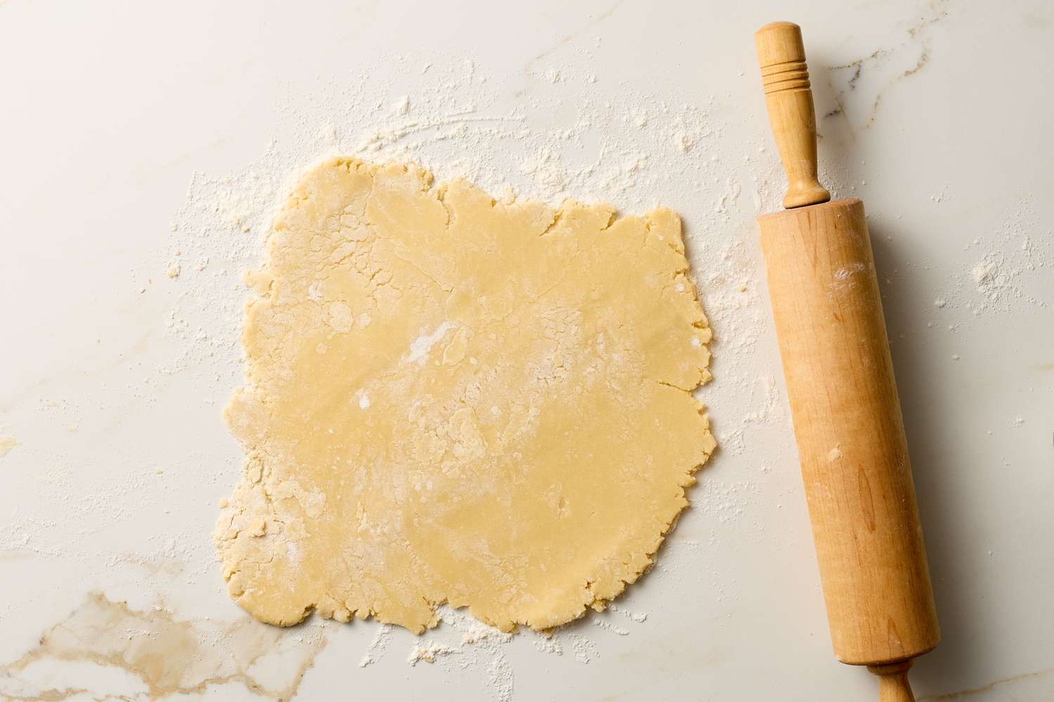 Rolledout cookie dough with a wooden rolling pin on a floured surface