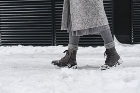 A person walking through a snowy street wearing boots and winter clothing only the lower part of their body is visible