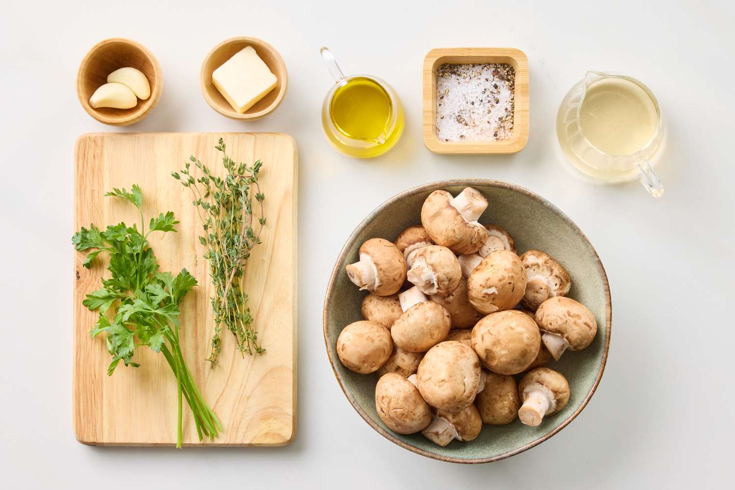 Ingredients for sauted mushrooms including a bowl of mushrooms herbs butter garlic olive oil salt pepper and white wine