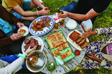 people around an outdoor table with several desserts on it