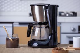 A coffee machine on a kitchen counter with a jar of ground coffee and a spoon nearby