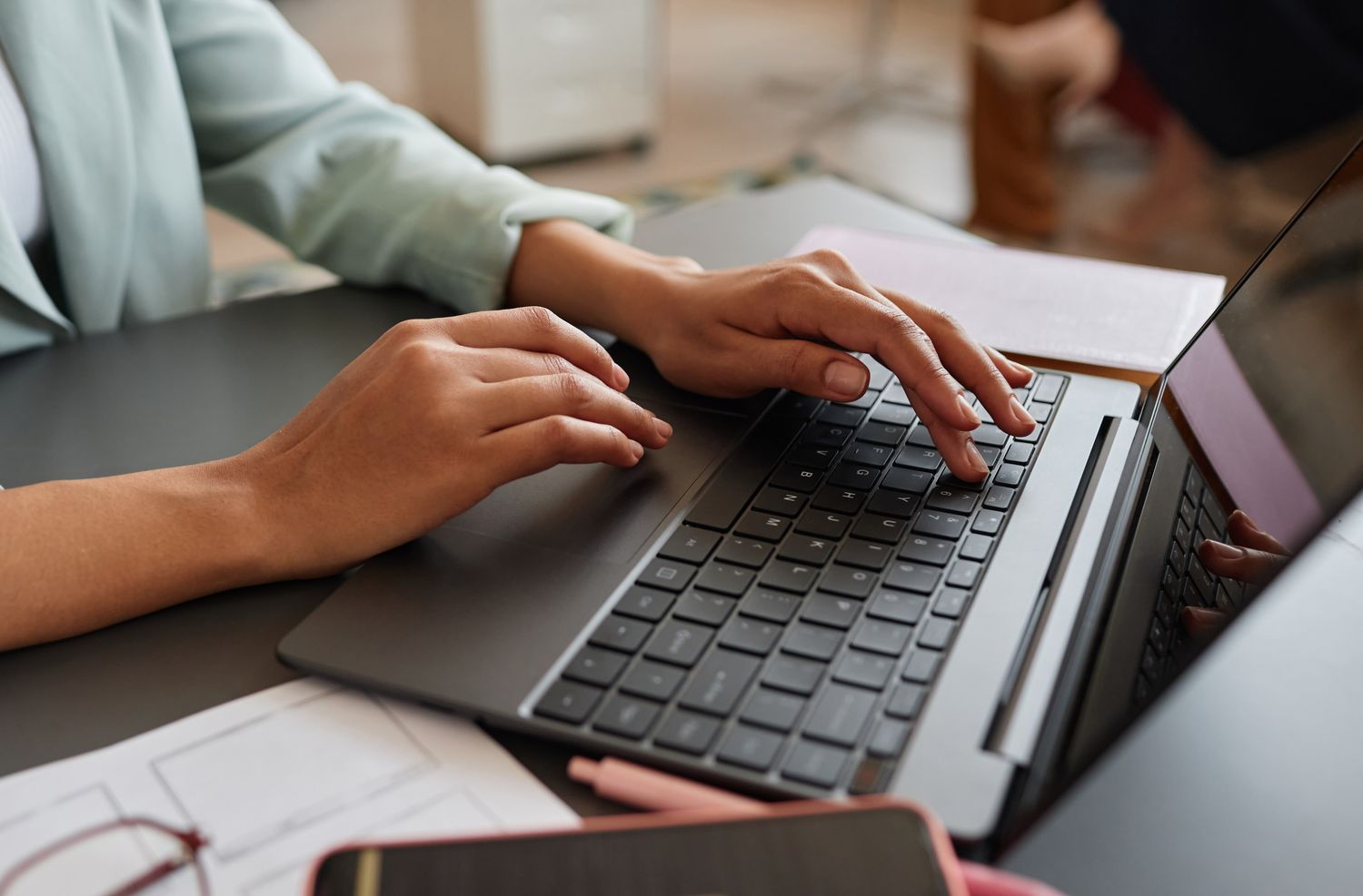 A person typing on a laptop keyboard at a desk with office supplies nearby