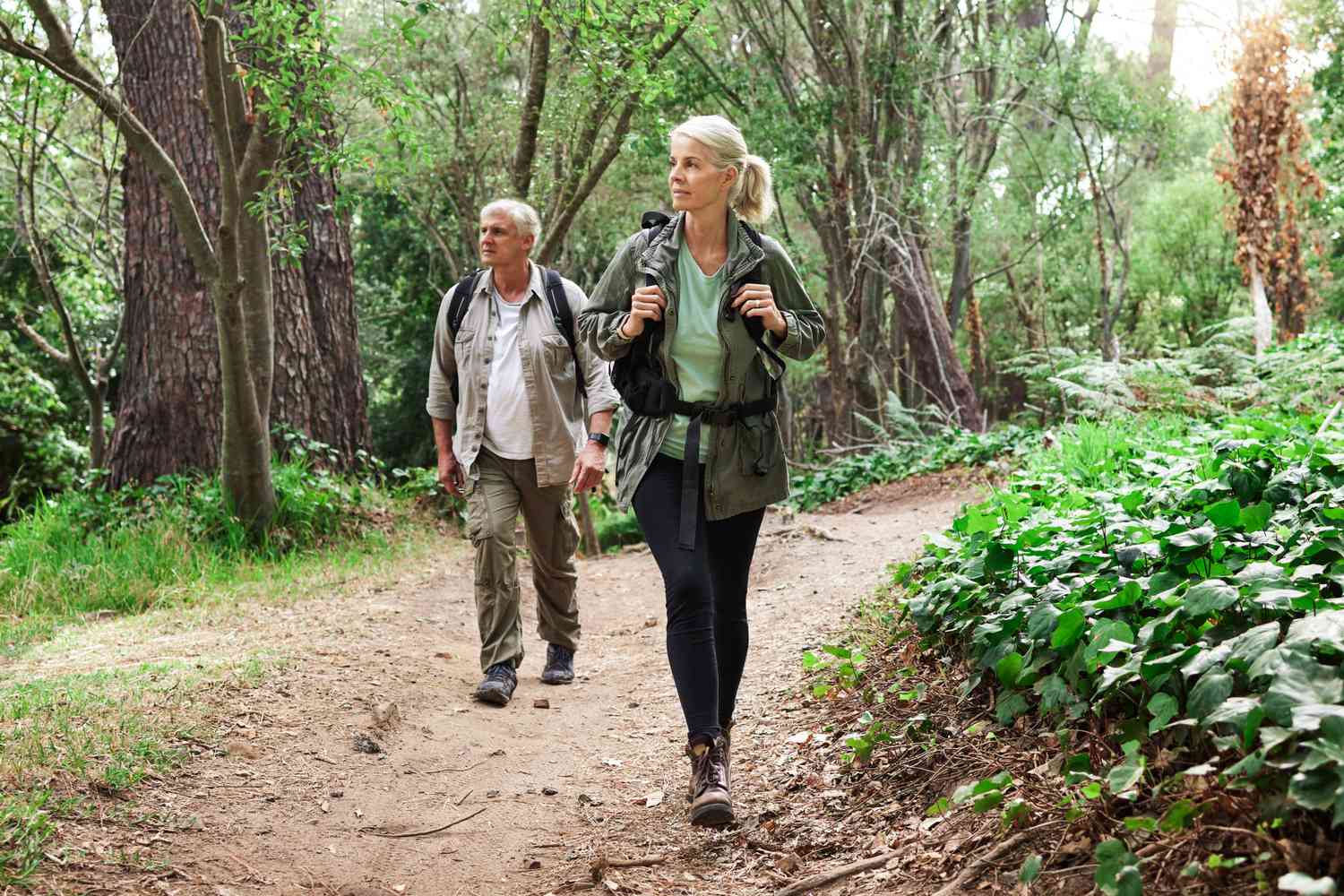A mature caucasian couple out for a hike together. Senior man and woman smiling and walking in a forest in nature