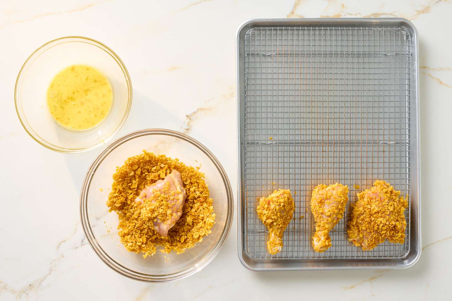 Cornflakecrusted chicken preparation with coated chicken pieces on a tray and ingredients in bowls