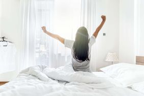 Person stretching on a bed in a bright room with curtains
