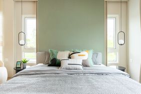 Stylish bedroom with green accent wall two windows pendant lights and a wellorganized bed with decorative pillows