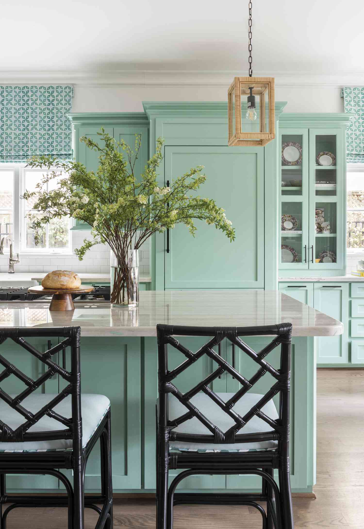 Kitchen design by Creative Tonic Design | Photography by Julie Soefer: mint-green cabinetry, rattan lighting, black bamboo barstools, and patterned Roman shades create a fresh, coastal feel.