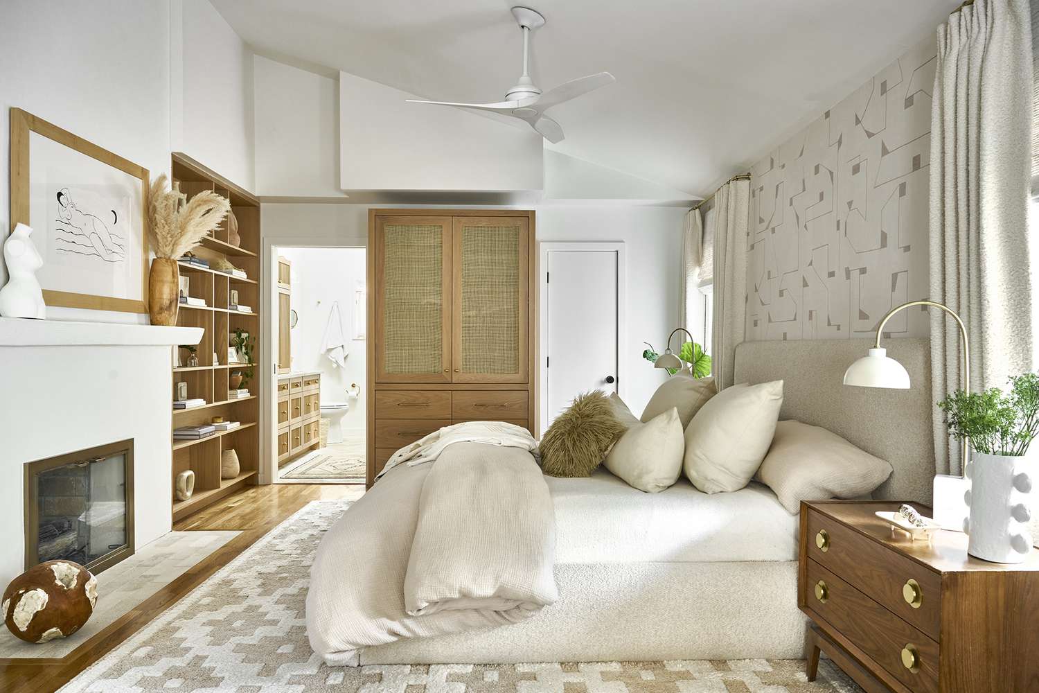 A white and brown primary bedroom with wooden accents and a geometric patterned wool rug.