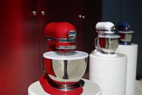 A red stand mixer displayed on a pedestal with other mixers in the background