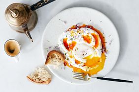 A plate with poached eggs topped with yogurt and spicy butter accompanied by toast a fork and a coffee cup