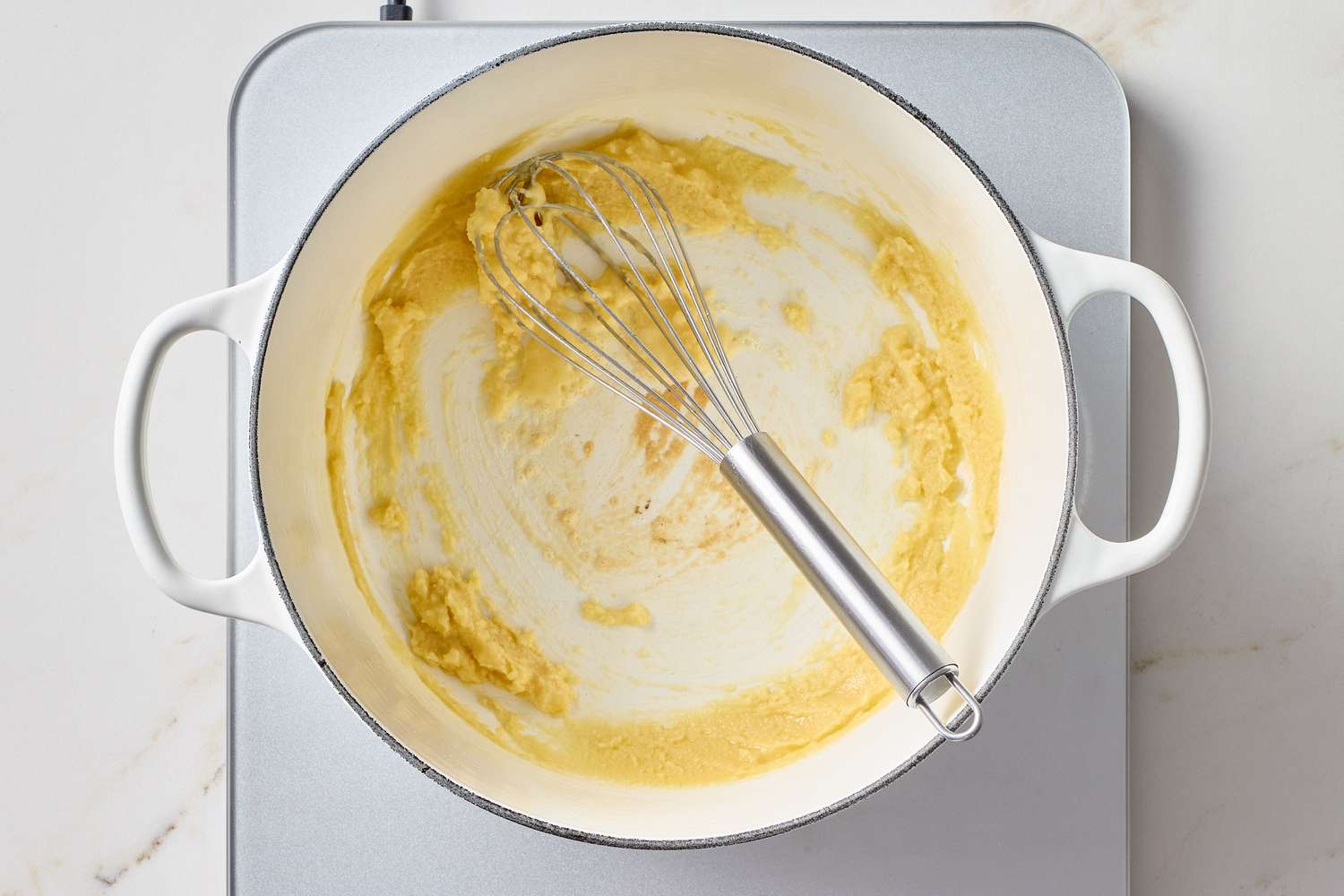 A whisk in a white pot containing melted butter and flour mixture