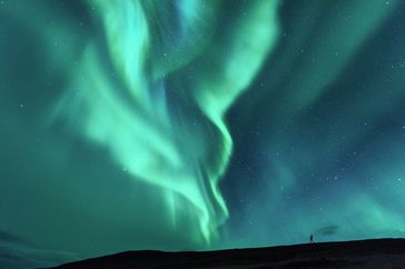 Person standing in a field under a sky illuminated by the northern lights