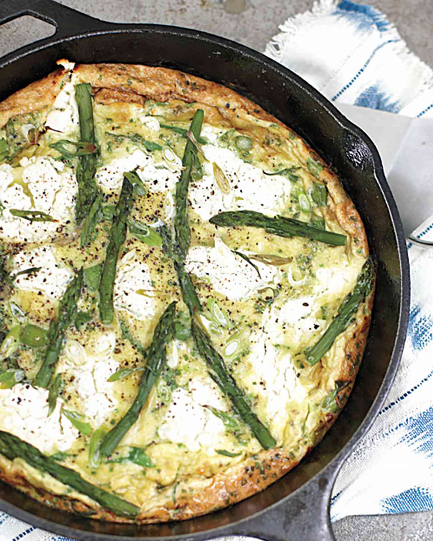 overhead view of a frittata with asparagus, goat cheese, and herbs