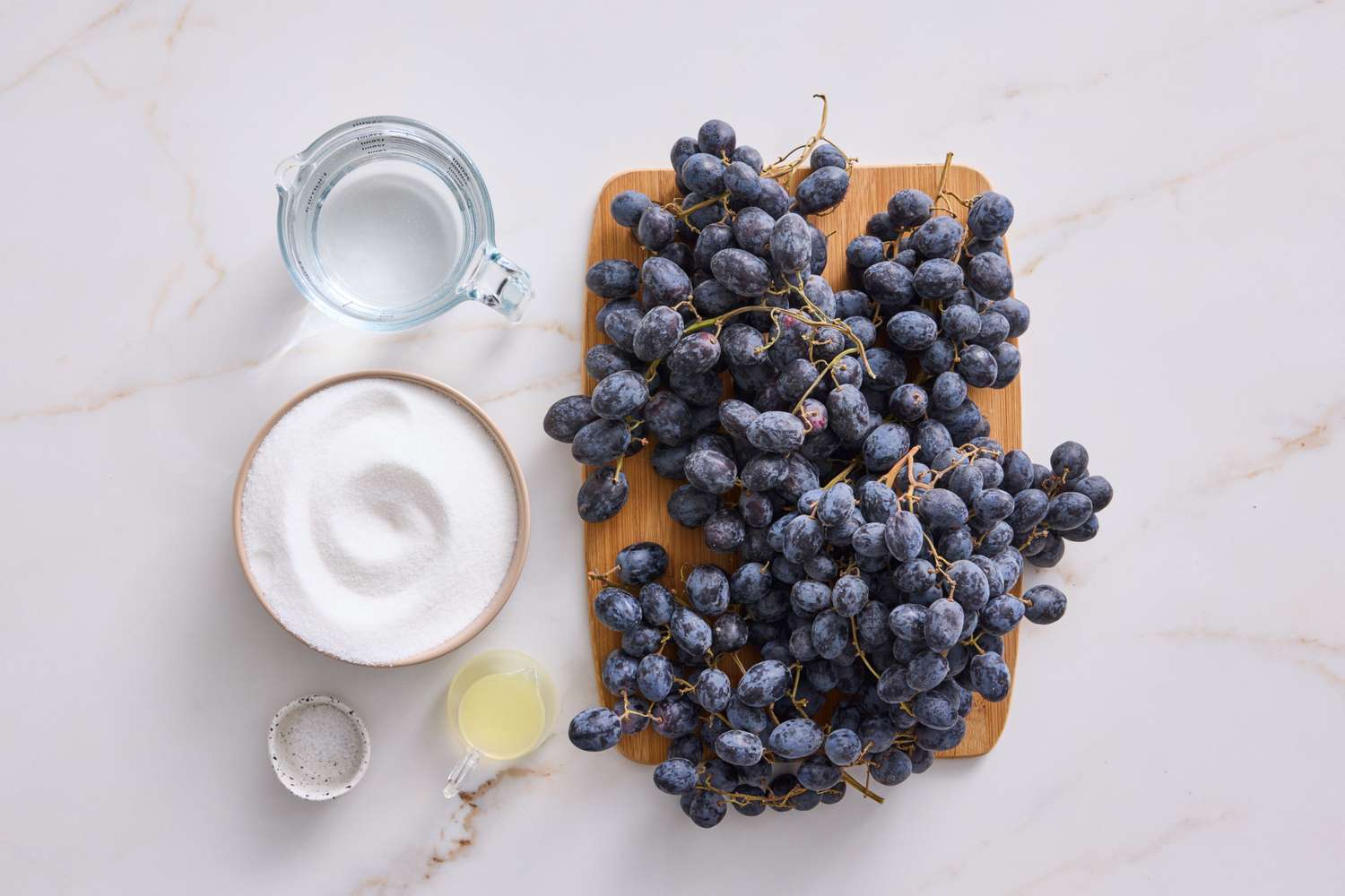 Ingredients for a basic jelly recipe displayed on a marble surface including grapes sugar water lemon juice and salt