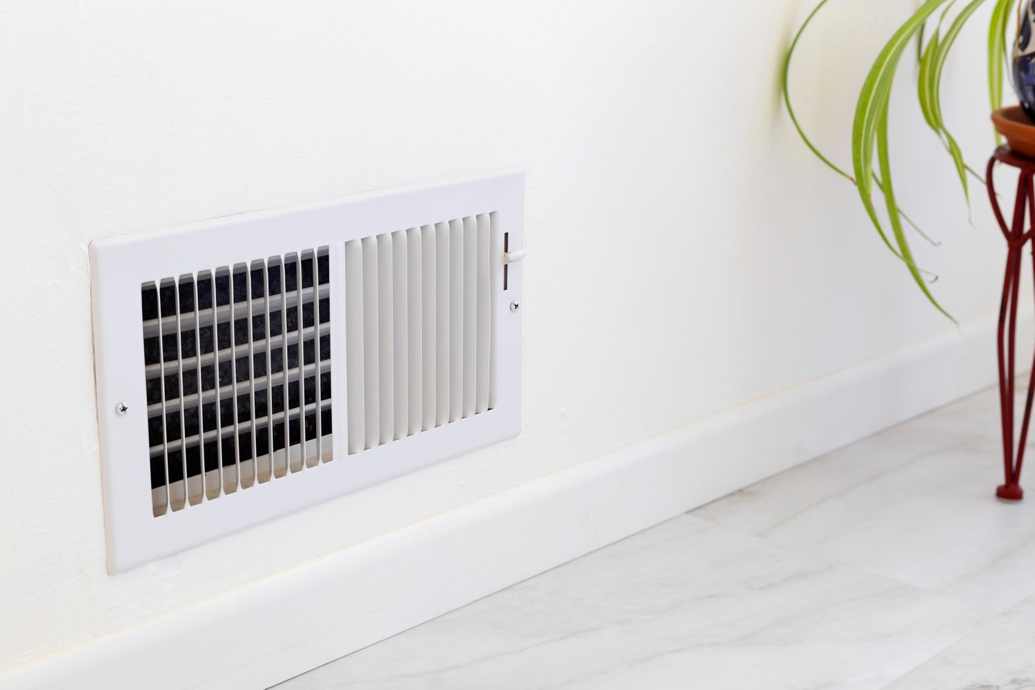 A wallmounted air vent with visible slats and a nearby green plant