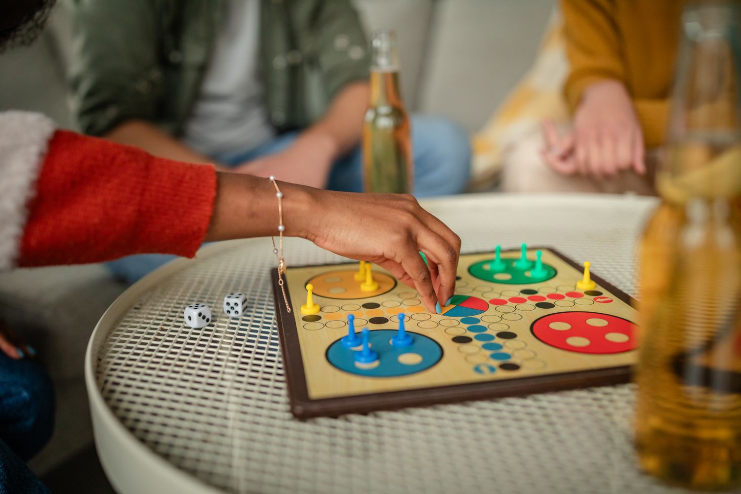 A hand moves a piece on a board game with other players sitting around a table