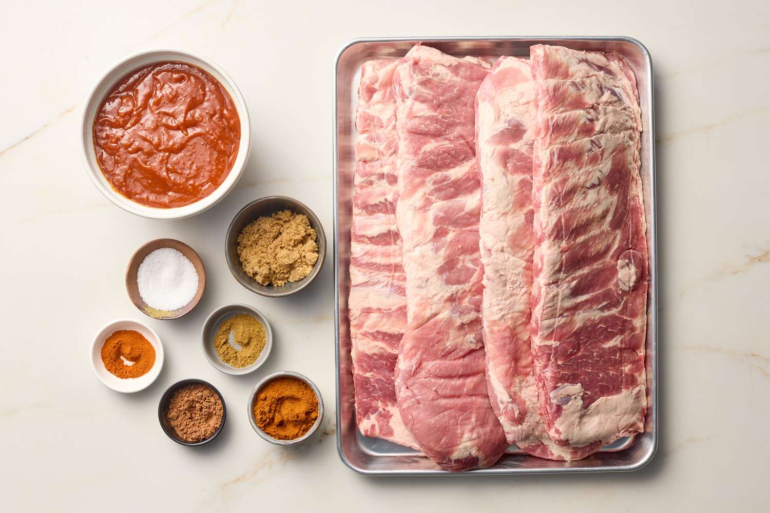 Ingredients for oven-roasted ribs with barbecue sauce including raw ribs, sauces, spices, and seasonings