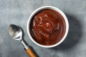 A bowl of chocolate pudding with a spoon next to it on a gray surface
