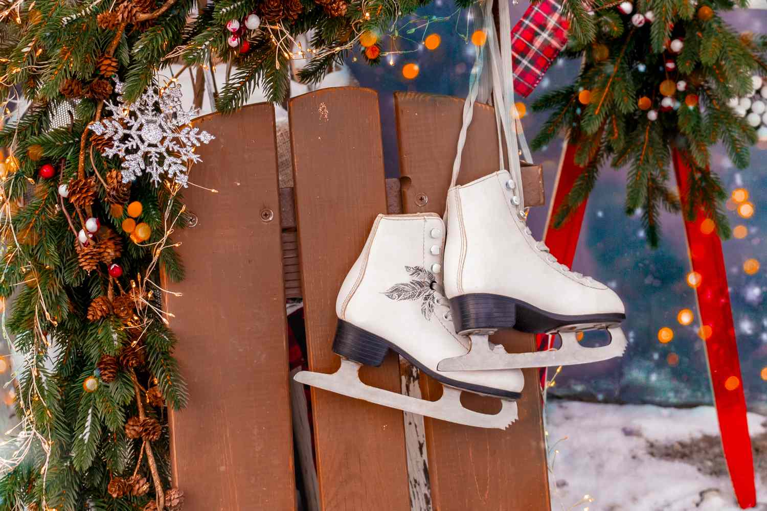 Pair of ice skates hanging on a wooden board surrounded by festive decorations including greenery and ornaments