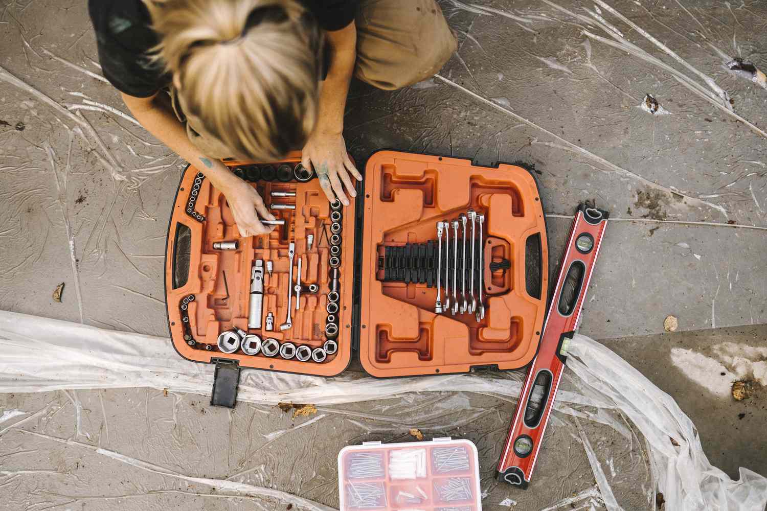 A person organizing tools in a toolbox on the ground with a level to the side