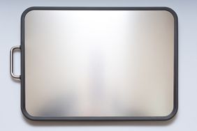 A stainless steel cutting board with a handle on the left