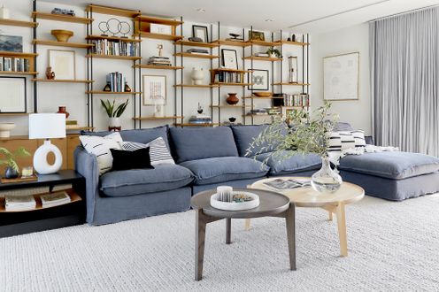 A modern living room with a blue sectional sofa minimalist shelves and a neutral carpeted floor