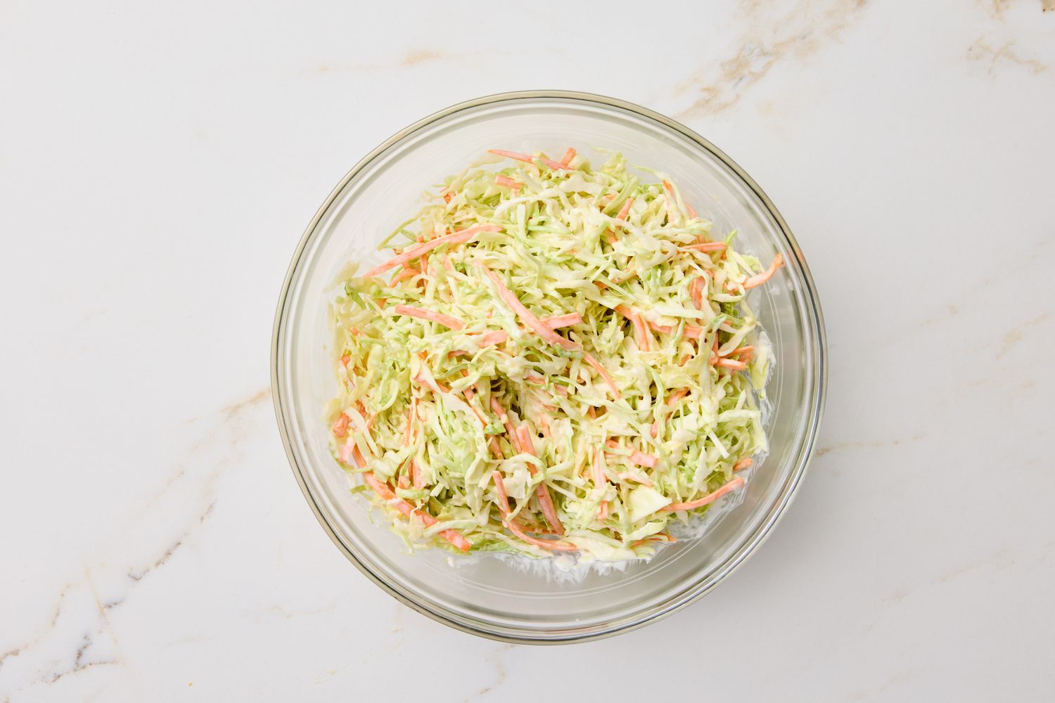 Bowl of coleslaw with shredded cabbage and carrots on a white surface