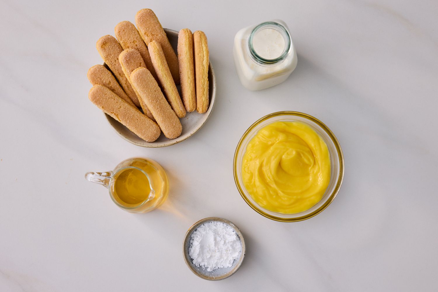 Ingredients for making lemon trifle including ladyfinger biscuits lemon curd powdered sugar and milk arranged on a surface