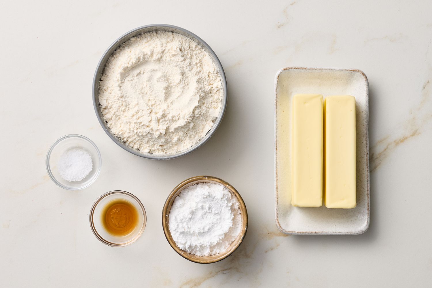Ingredients for making shortbread cookies displayed on a table including flour butter powdered sugar vanilla and salt
