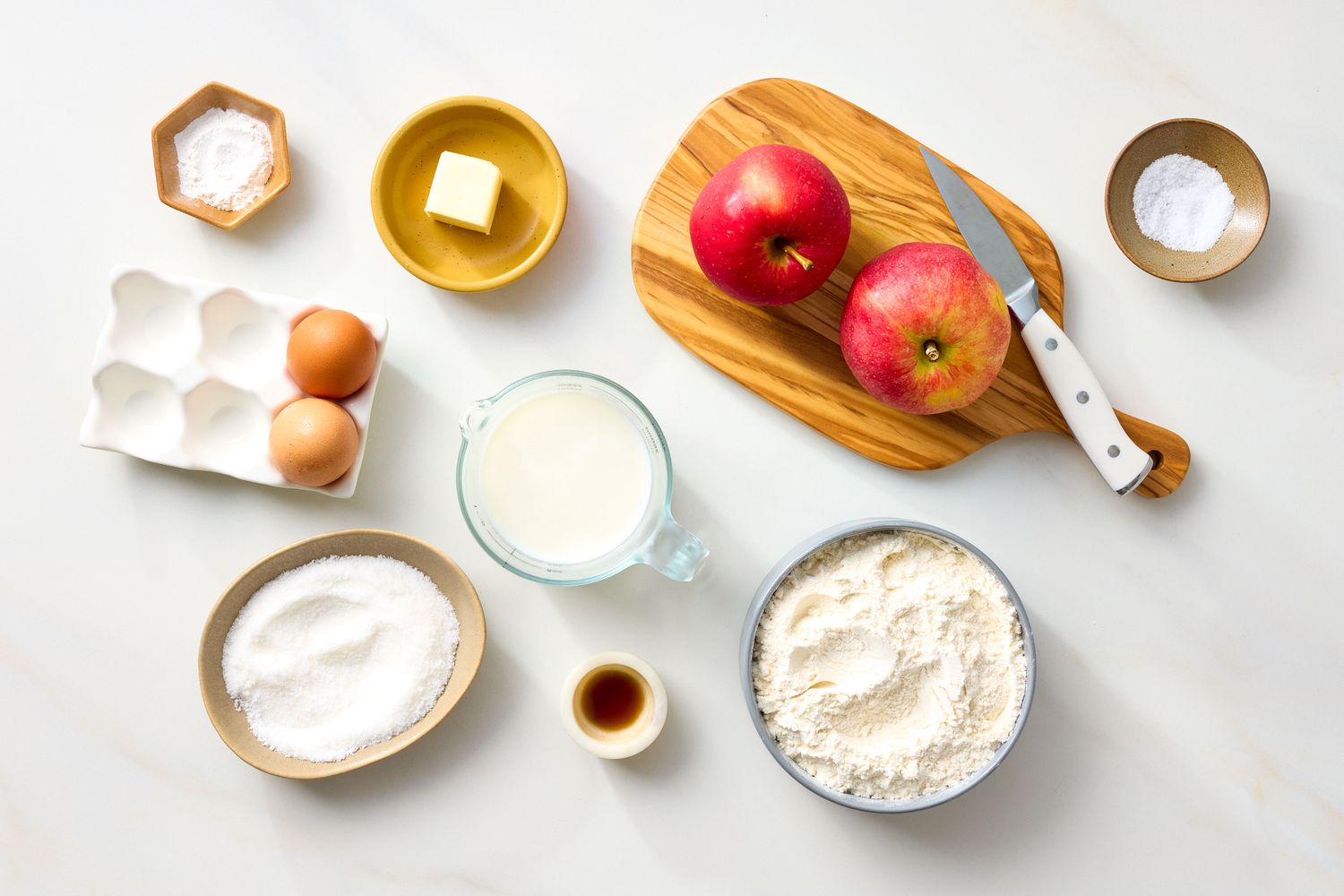 Ingredients arranged for making apple fritters including apples flour eggs butter milk vanilla and spices displayed on a counter