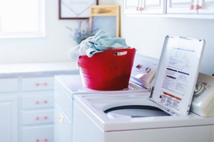 Laundry room with a red basket holding clothes on top of a washing machine lid open showing instructions panel cozy home environment