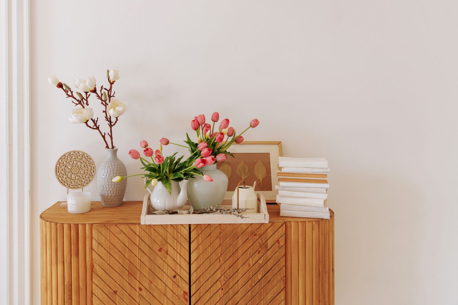 A wooden sideboard with decorative vases flowers books and framed art