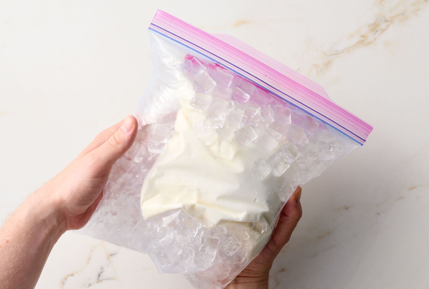 Hands holding a sealed plastic bag containing ice and a smaller bag of ingredients