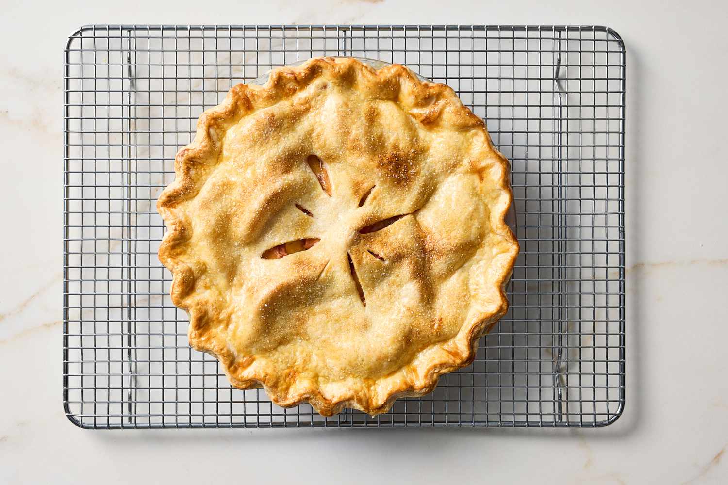 A baked pie with a crimped edge and steam vents on top cooling on a wire rack