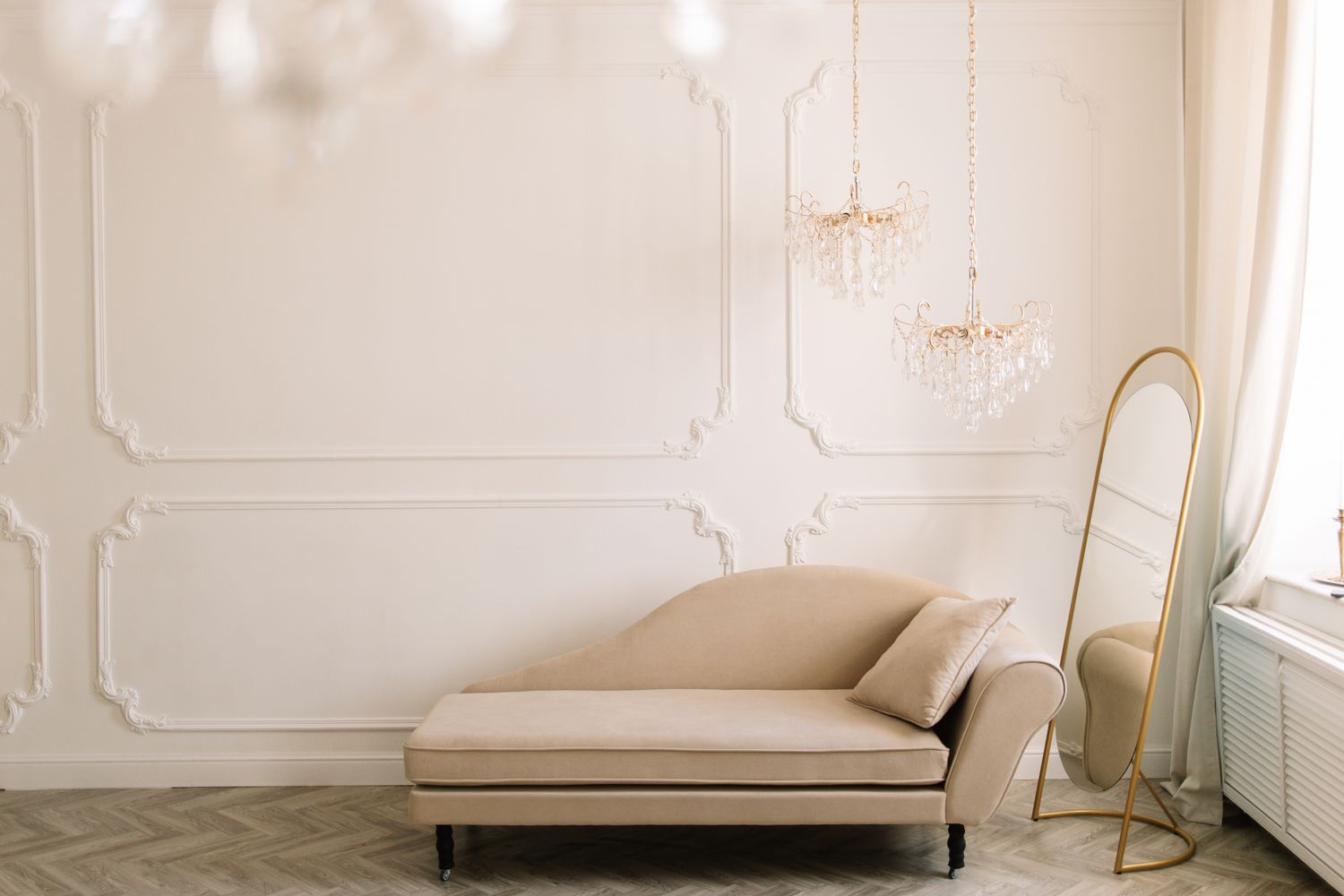 Elegant room with a chaise lounge, standing gold mirror, and chandeliers