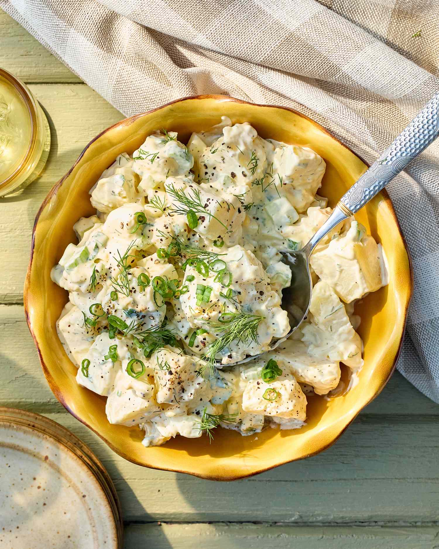 A bowl of potato salad topped with green garnish served on a wooden table