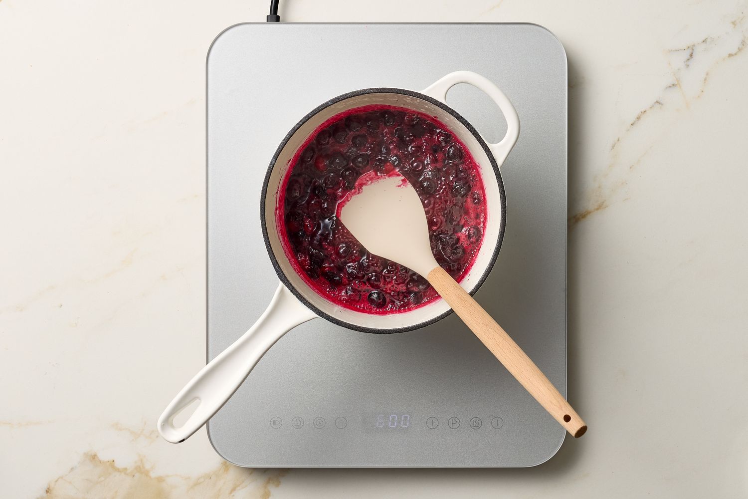 Pot containing blueberry mixture on a hot plate with a spatula inside